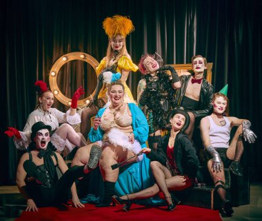 Kabare grubu kırmızı halıda büyüleyici retro enerjiyle neşe dolu pozlar veriyor. Cesur makyajlı erkekler ve kadınlar. Kabare, gösteri, sirk, retro, vintage, performans konsepti.