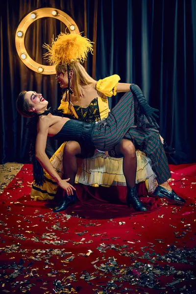 Retro kabare ikilisi, erkek ve kadın sanatsal poz veriyor. Kırmızı halıda spot ışıkları ve dramatik stiliyle flört havası var. Kabare, gösteri, sirk, retro, vintage, performans konsepti.