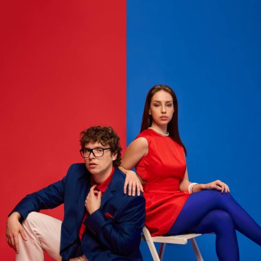 Tarz sahibi bir çift, oturuyorlar ve güvenle poz veriyorlar. Renk engellenmiş kırmızı ve mavi ortamda. Güç ve birliği yansıtıyorlar. İnsan duyguları, ilişkisi, yaşam tarzı kavramı.