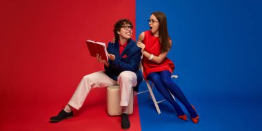 Heyecanlı ve şok olmuş yüzlü kadın ve erkek kitap okuyor, bölünmüş kırmızı ve mavi arka plana karşı neşeli anları paylaşıyorlar. İnsan duyguları, ilişkisi, yaşam tarzı kavramı