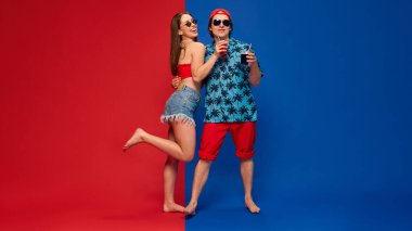 Kadın bacak kaldırıyor ve tropikal kıyafetli adama sarılıyor. Renkli arka plana karşı neşeli ifadeler takınıyor. İnsan duyguları, ilişkisi, yaşam tarzı kavramı