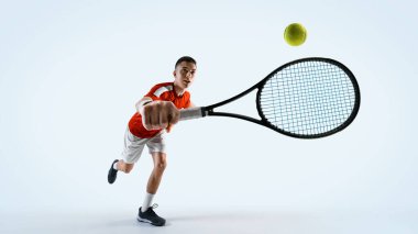 Genç adamın dinamik görüntüsü, tenis oyuncusu topa önden vuruyor, beyaz stüdyo arka planına karşı hız ve hassasiyet gösteriyor. Spor, oyun, turnuva, pratik, gençlik kavramı