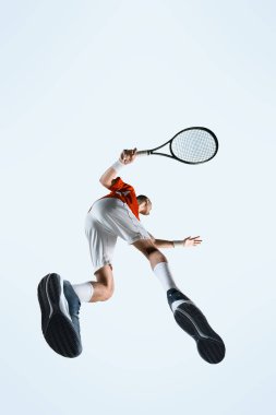 Yoğunlaşmış adamın alt görüntüsü, tenis atleti beyaz stüdyo arka planına doğru uçuşun ortasında güçlü bir ters hareketle yakalandı. Spor, oyun, turnuva, pratik, gençlik kavramı