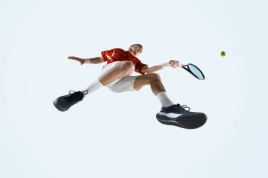 Odaklanmış genç adamın alt görüntüsü, üniformalı bir tenisçi top ve raketle hareket halinde, yoğun oyun anında beyaz stüdyo arka planına karşı. Spor, oyun, turnuva, pratik kavramı