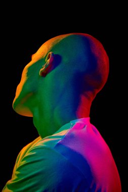 Beyaz tişörtlü, arkası açık kel bir adamın portresi yukarı ve solda, çok renkli neon ışıklı koyu bir arka planda. Erkek güzelliği, moda, tarz, gençlik kültürü kavramı