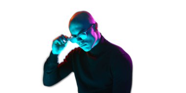 Siyah balıkçı yaka yakalı, güneş gözlüklü ve mavi ve pembe ışıklı beyaz arka planda aşağı bakan kendinden emin genç kel bir adam. Erkek güzelliği, moda, tarz, gençlik kültürü kavramı