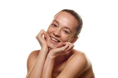 Parlak, pürüzsüz bir teni ve çilleri olan, gülümseyen, beyaz arka planda poz veren genç bir kadının portresi. Doğal güzellik kavramı, güven, kozmetik ve kozmetik, sağlık