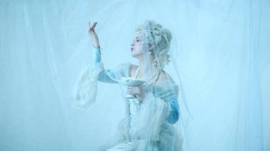 Ortaçağ düşesi gibi zarif genç bir kadın klasik korse giymiş açık mavi arka planda inci kolye kaldırıyor. Kraliyet kavramı, zarafet, güzellik ve moda, çağların karşılaştırması.