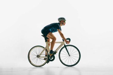 Bisikletle hareket eden profesyonel bisikletçi, beyaz arka planda tek başına giden genç bir adamın yan görüntüsü. Spor anlayışı, rekabet, aktif yaşam tarzı, dayanıklılık