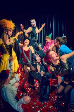 Kabare göstericileri kırmızı halıda klasik kostümler içinde dramatik ifadeler ve sahne aksesuarlarıyla poz veriyorlar. Kabare, gösteri, sirk, retro, vintage, performans konsepti.