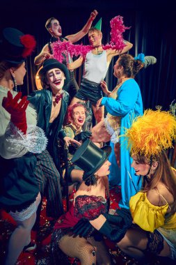 Kabare göstericileri, gülen erkekler ve kadınlar, kırmızı halıda dramatik ifadeler ve sahne aksesuarlarıyla klasik kostümler içinde poz veriyorlar. Kabare, gösteri, sirk, retro, vintage, performans konsepti.