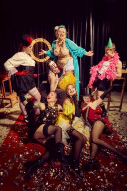 Eksantrik, klasik tarz kıyafetler giymiş erkek ve kadınlar konfeti serpiştirilmiş kırmızı halı üzerinde dramatik bir şekilde poz verirler, retro sirkin anlamlı ruhu, kabare gösterisi. Kabare, gösteri, sirk, retro, vintage