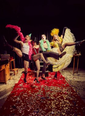 Kırmızı halıda dramatik ifadeler ve sahne aksesuarlarıyla dinamik poz veren dört kabare sanatçısından oluşan bir grup. Kabare, gösteri, sirk, retro, vintage, performans konsepti.