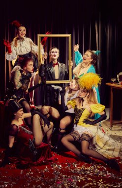 Dramatik ve kaprisli klasik kostümlerin karışımı kabare sanatçıları konfetiyle kaplı kırmızı halının üzerinde altın çerçeve etrafında toplandılar. Kabare, gösteri, sirk, retro, vintage, performans konsepti.