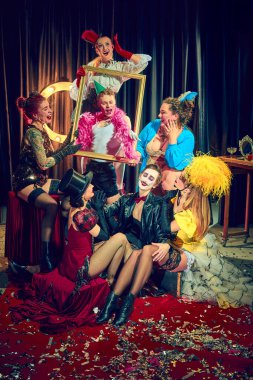 Klasik sirk ve kabare kıyafetleri içinde kırmızı halıdaki altın çerçeveli göstericiler abartılı duygular sergiliyorlar. Kabare, gösteri, sirk, retro, vintage, performans konsepti.