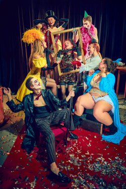 Konfeti serpiştirilmiş kırmızı halıda poz veren klasik kostümlü tiyatrocular, altın çerçevenin etrafında etkileşime geçiyorlar. Kabare, gösteri, sirk, retro, vintage, performans konsepti.