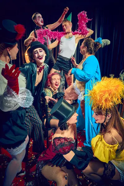 Kabare göstericileri, gülen erkekler ve kadınlar, kırmızı halıda dramatik ifadeler ve sahne aksesuarlarıyla klasik kostümler içinde poz veriyorlar. Kabare, gösteri, sirk, retro, vintage, performans konsepti.