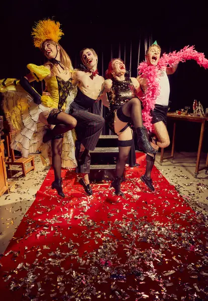Kırmızı halıda poz veren dört enerjik kabare sanatçısı konfetilerle kaplı, eski moda kıyafetleriyle neşeli, tiyatral ifadeler sergiliyorlar. Kabare, gösteri, sirk, retro, vintage, performans konsepti.