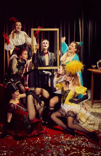 Dramatik ve kaprisli klasik kostümlerin karışımı kabare sanatçıları konfetiyle kaplı kırmızı halının üzerinde altın çerçeve etrafında toplandılar. Kabare, gösteri, sirk, retro, vintage, performans konsepti.