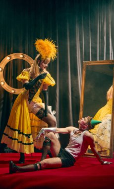 Kırmızı halıyla kırmızı halı üzerinde, biri diğerinin üzerinde dramatik bir şekilde duran iki klasik kostümlü sanatçı arasındaki tiyatro etkileşimi. Kabare, gösteri, sirk, retro, vintage, performans konsepti