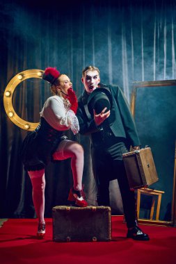 Kabare sanatçıları, kadın ve erkek, dramatik ifadeler ve sahne aksesuarlarıyla kırmızı halıda klasik kostümlerle poz veriyorlar. Kabare, gösteri, sirk, retro, vintage, performans konsepti.