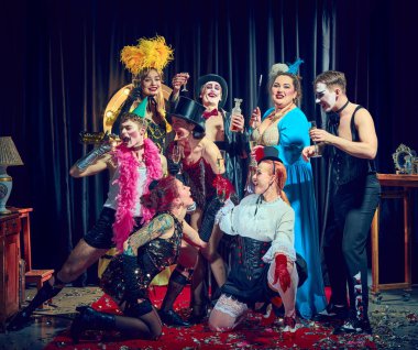 Neşeli kabare kadehleri kırmızı eldivenli şampanya bardakları, korse tüyleri ve konfeti tutuyor. Kabare kavramı, gösteri, retro, kutlama, mizah, tost, performans, parti, gece hayatı.