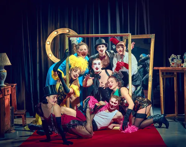 Renkli vintage kostümlü ve dramatik makyajlı kabare sanatçıları kırmızı halıdaki büyük altın çerçevenin etrafında dramatik bir poz veriyorlar. Kabare, gösteri, sirk, retro, vintage