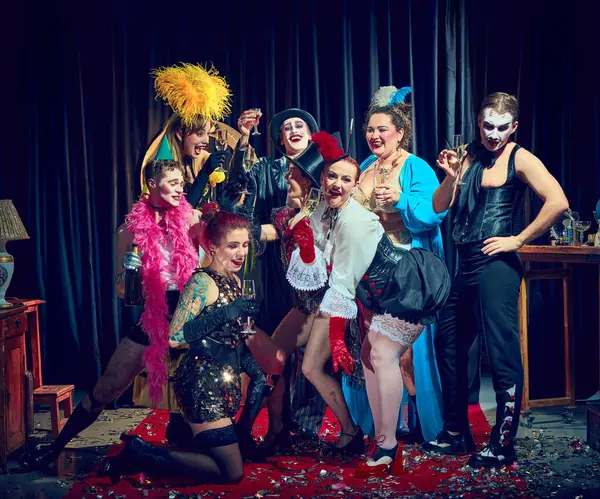 Korse giymiş kabare grubu kırmızı halı konfetisinin üzerinde bardaklarla kadeh kaldırıyor. Kabare, gösteri, klasik kutlama, performans, mizah, içki, sirk, tiyatro konsepti.