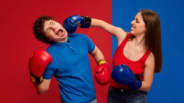 Dramatik genç adam ve kadın, boks eldiveni giyen ve yüzüne yumruk atan çift, canlı kırmızı ve mavi arka plana karşı abartılı ifadeler kullanıyor. Mizah anlayışı, spor, tepki.