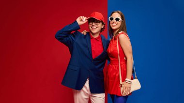 Parlak kıyafetlerle gülümseyen, kendine güvenen, şapkalı, kırmızı mavi arka planda golf topu tutan çift. İnsan duyguları kavramı, ilişki, yaşam tarzı, moda, spor