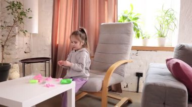 5 yaşında bir kız, evinde sandalyede oturmuş, konsantrasyonlu renkli kille oynamaya odaklanmış. Yaratıcı oyunun özü. Çocukluk kavramı, oyun, yaratıcılık, eğitim