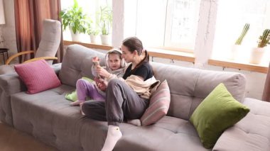 Sevgi dolu bir aile. Anne ve kızı evde birlikte vakit geçiriyorlar. Kanepede oturup, kulaklık takıp akıllı telefona bakmak. Dijital eğlence ya da öğrenme. Çocukluk kavramı