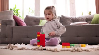 Nişanlı bir çocuk halının üzerinde oturuyor, renkli blokları olan bir bina. Yaratıcı yapı ve oyun. Çocukluk kavramı, oyun, yaratıcılık, yapı, ev, eğlence.