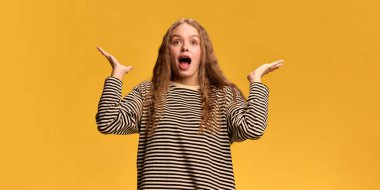 Şaşırdığını ve şaşırdığını ifade eden genç bir kadın ağzı açık ve elleri sarı stüdyo geçmişine karşı inançsızlık jesti olarak havada. İnsan duyguları kavramı, yaşam tarzı, sürpriz, doğallık..