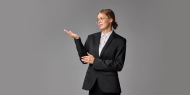 Profesyonel bir kadın, gri stüdyo geçmişine karşı sunum yapıyormuş gibi hareket ediyor. İş yeri iletişimi, yaşam tarzı, duygu, sunum, kariyer geliştirme kavramı