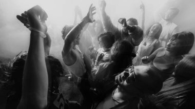 Elleri havada dans eden, enerjik bir atmosfer yaratan siyah ve beyaz bir kalabalık fotoğrafı. Parti anlayışı, gençlik, gece kulübü, kutlama.