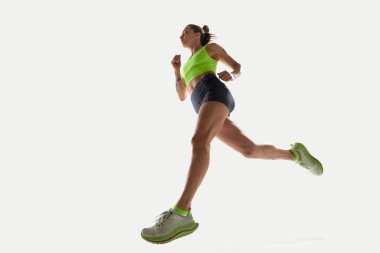 Düşük açılı, yeşil bluzlu, beyaz arka planda siyah şortlu, sportif genç bir kadının görüntüsü. Spor, rekabet, aktif yaşam tarzı, eylem, hareket, hız, performans kavramı.