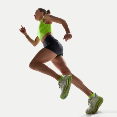 Yeşil bluzlu atletik kadın beyaz stüdyo ortamında koşarken azimle yukarı bakıyor. Spor kavramı, rekabet, aktif yaşam tarzı, güven, güç, eylem, kişisel olarak en iyisi.