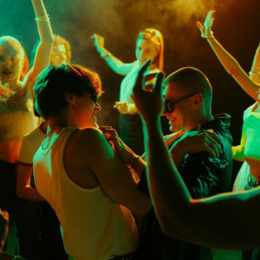 Bir grup insan renkli ışıklandırmalı bir partide enerjik bir şekilde dans ediyor. Konser konsepti, müzik, parti, Igbt. Ad