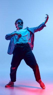 Tam güçle dans eden bir adamın dinamik fotoğrafı güçlü poz verirken ve neon ışıkta, arka plandaki değişime karşı ifade edici bir yüz ifadesi sahnedeki performansı gibi. Gençlik kavramı, insan duyguları, enerji