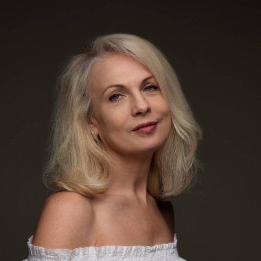 Kendine güvenen olgun bir kadının portresi pürüzsüz ciltli ve kaldırılmış bir yüz. Karanlık stüdyo geçmişine gülümseyen bir ifadeyle. Kaldırma efekti, yaşlanma önleme, olgun cilt bakımı, estetik ameliyat konsepti