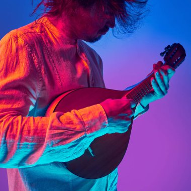 Canlı kırmızı ve mavi sahne ışıkları altında mandolin çalan bir adam gradyan stüdyo arka planına karşı. Ritmik akorlar. Anlamlı müzik ve ses enerjisi kavramı, geleneksel dans motifleri.