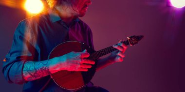 Koyu renk tişörtlü bir adam arka planda neon ışıkları ve arka planda sahne atmosferi olan folk telli bir enstrüman çalıyor. Müzik aletinin detaylı fotoğrafı. Canlı halk müziği kavramı, performans