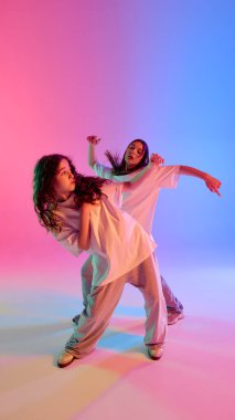 İki genç dansçının dinamik fotoğrafı, arka planda canlı ışıklandırma altında, gevşek kıyafetlerle hip hop yapıyorlar. Anlamlı ritim, özgürlük ve modern sokak sanatı kavramı.
