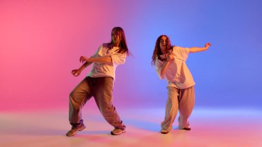 İki genç kız, yetenekli dansçılar pembe ve mavi ışıklar altında renkli stüdyo geçmişine karşı sokak hareketleri yapıyorlar. Müzik, ritim, hareket ve kültürel kimlik kavramı.