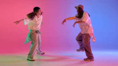 Hip hop ikilisi, genç yetenekli kızlar pembe ve mavi neon ışıkları altında dinamik hareketlerle dans ediyorlar. Müzik kavramı, serbest stil, ritim, cesaret ve sokak hareketi.