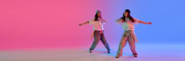 İki kız, parlak neon ışıkları altında senkronize hip hop performansı sergiliyor. Gradyan arka planda, giriş metninde negatif alan var. Pankart. Takım çalışması, hareket ve gençlik kültürü kavramı