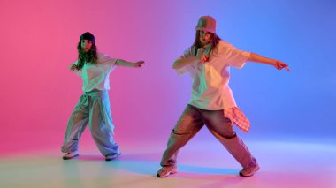 Hip hop dans ikilisi, parlak neon ışıklarının altında pembe ve mavi renk değişimine karşı poz veriyor. Dinamik fotoğraf. Spor, müzik, gösteri, hareket, güven ve gençlik kültürü kavramı.