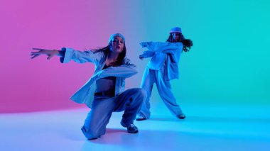 Genç hip hop dansçıları, şık sokak kıyafetleri giyen kızlar, Cyan gradyan arka planına karşı mavi ve pembe ışıklarla gösteri yapıyorlar. Müzik anlayışı, modern sokak tarzı ve cesur hareket.