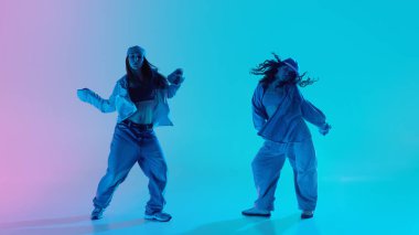 Genç hip hop dansçıları dans kıyafetleri içinde pembe ve turkuaz neon renkli arka plan altında poz veriyorlar. Müzik kavramı, modern moda, serbest stil enerji ve hareket.